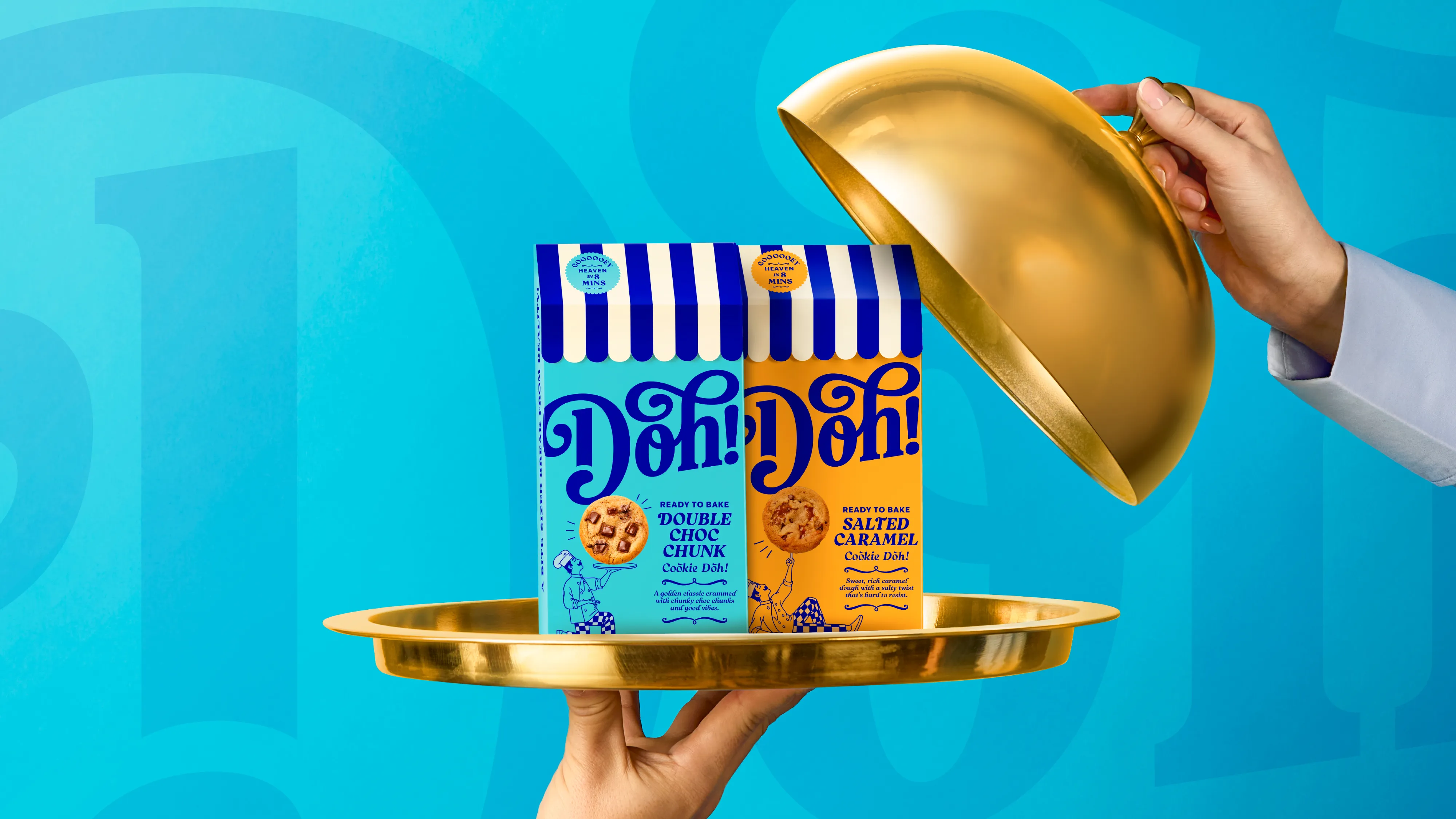 Two colorful Doh! cookie dough packages, Double Choc Chunk and Salted Caramel, on a gold serving tray with a hand lifting a gold cloche.