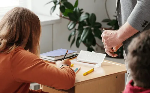 A girl writing on a paper on top of a table.