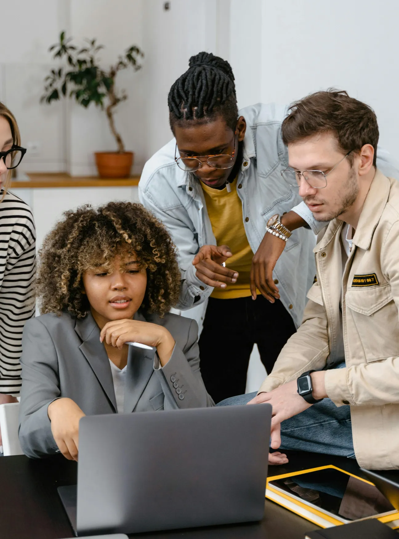 An image of four people talking to each other, where one person is showing something on a computer screen, pointing at it.