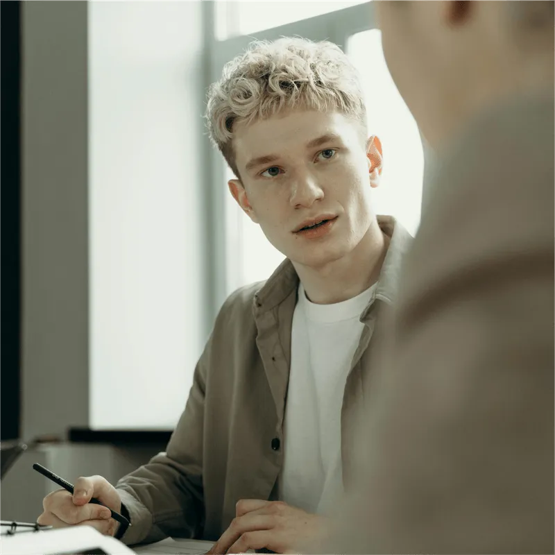 An image of a blond hair man talking to another person.
