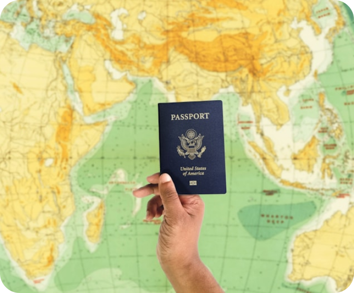 Hand holding a United States of America passport in front of a world map.