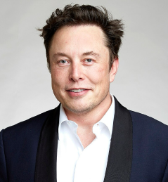 Man with dark hair wearing a white shirt and dark blazer, smiling against a plain gray background.