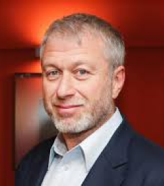 Middle-aged man with light gray hair and beard wearing a dark blazer and light shirt against a red background.