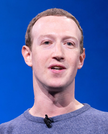 Man with short brown hair and fair skin wearing a gray shirt speaking in front of a blue background.