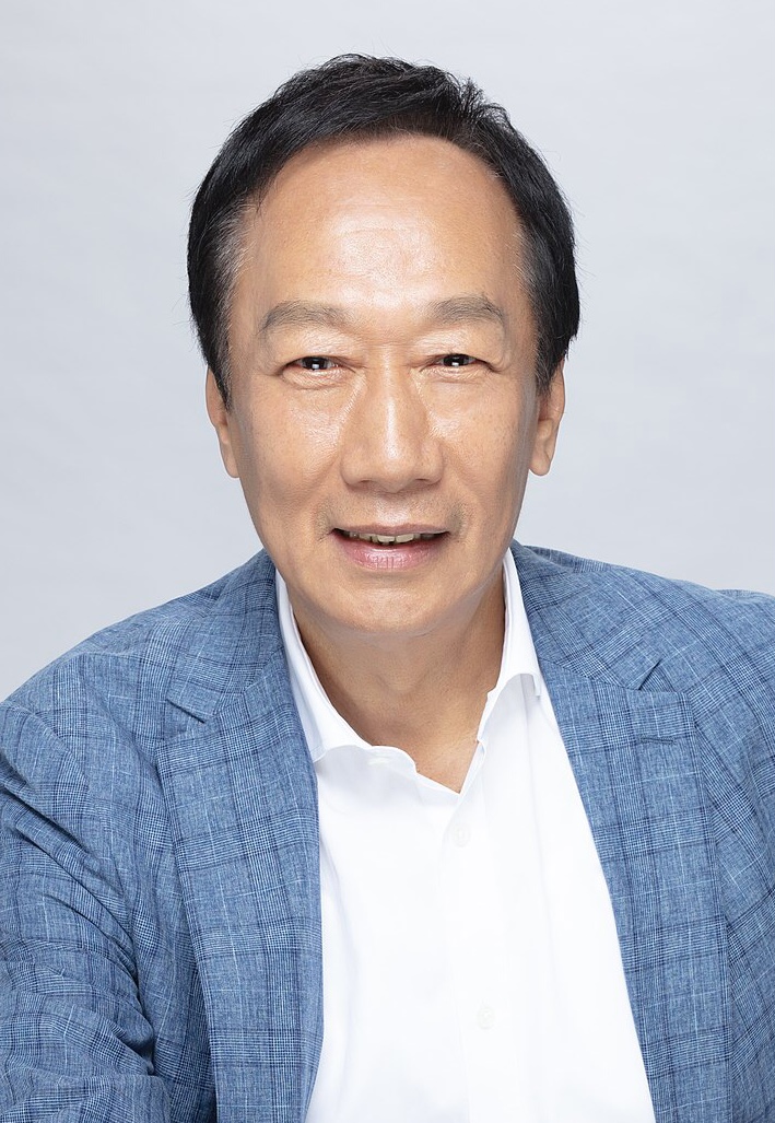 Middle-aged Asian man smiling, wearing a blue blazer and white shirt against a plain light background.