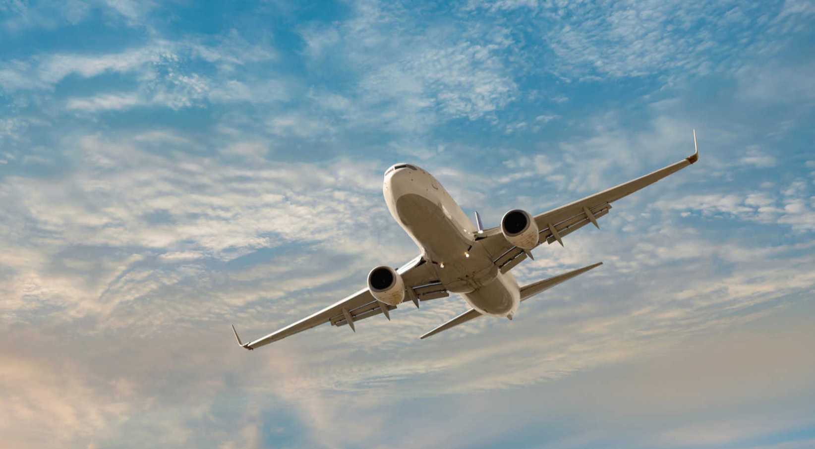 Commercial airplane flying overhead against a partly cloudy sky.