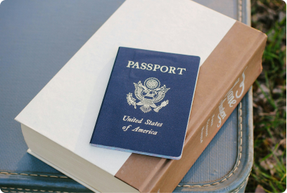 United States passport resting on top of a thick closed book with a brown spine, placed on a blue suitcase.
