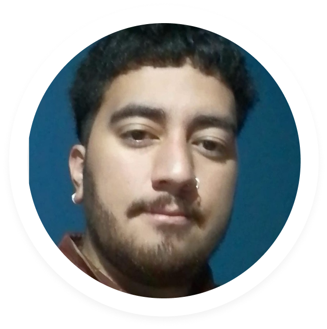 Close-up portrait of a young man with short curly hair, a beard, and nose and ear piercings against a solid blue background.
