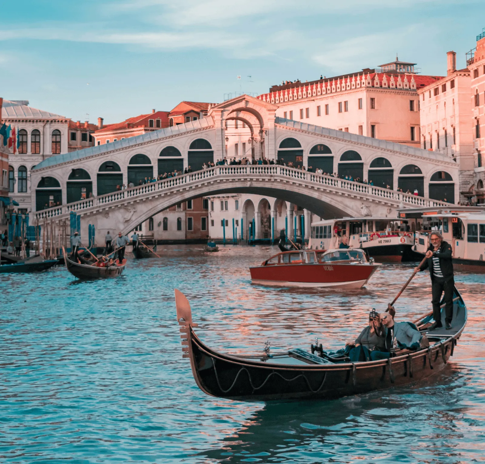 Gondola with two passengers and a gondolier in Venice canal near the Rialto Bridge at sunset.