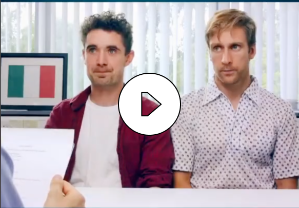 Two men sitting side by side at a table in a room with vertical blinds and a framed Italian flag in the background.