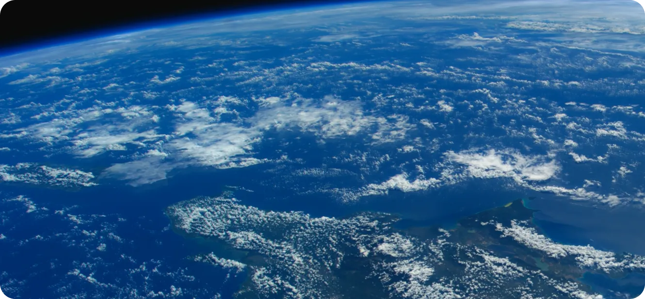 View of Earth from space showing a large landmass with scattered clouds over deep blue ocean and a faint atmospheric glow at the horizon.