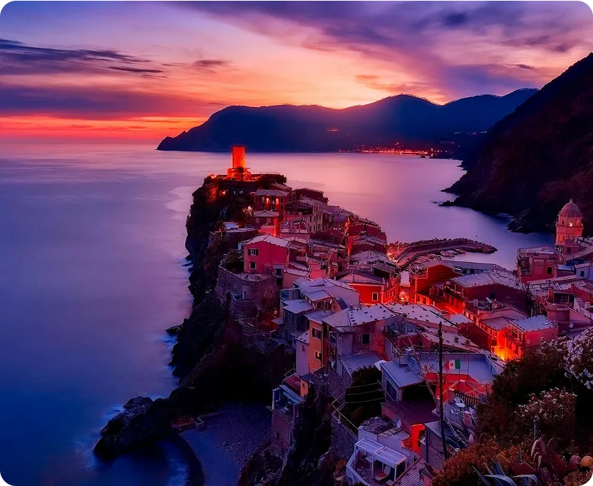 Coastal village perched on cliffs at sunset with colorful sky and calm sea.