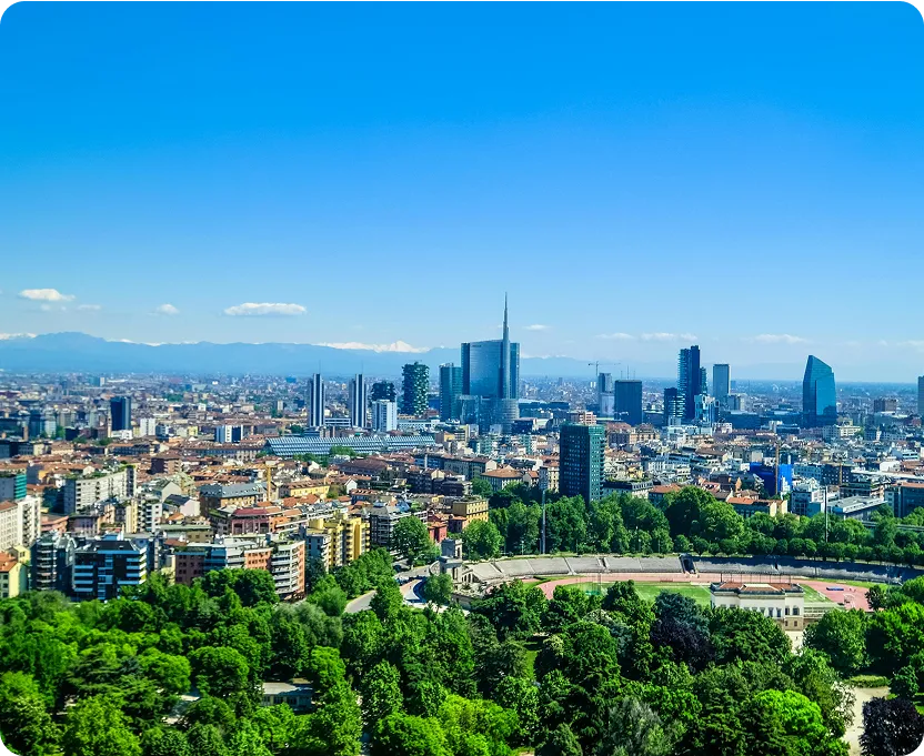 City skyline with modern skyscrapers behind a green park and a circular stadium under a clear blue sky.
