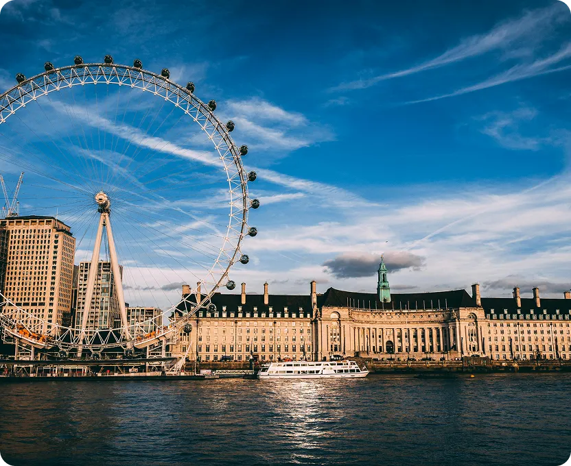London Eye Ferris wheel and historic building by the River Thames under a blue sky with scattered clouds.
