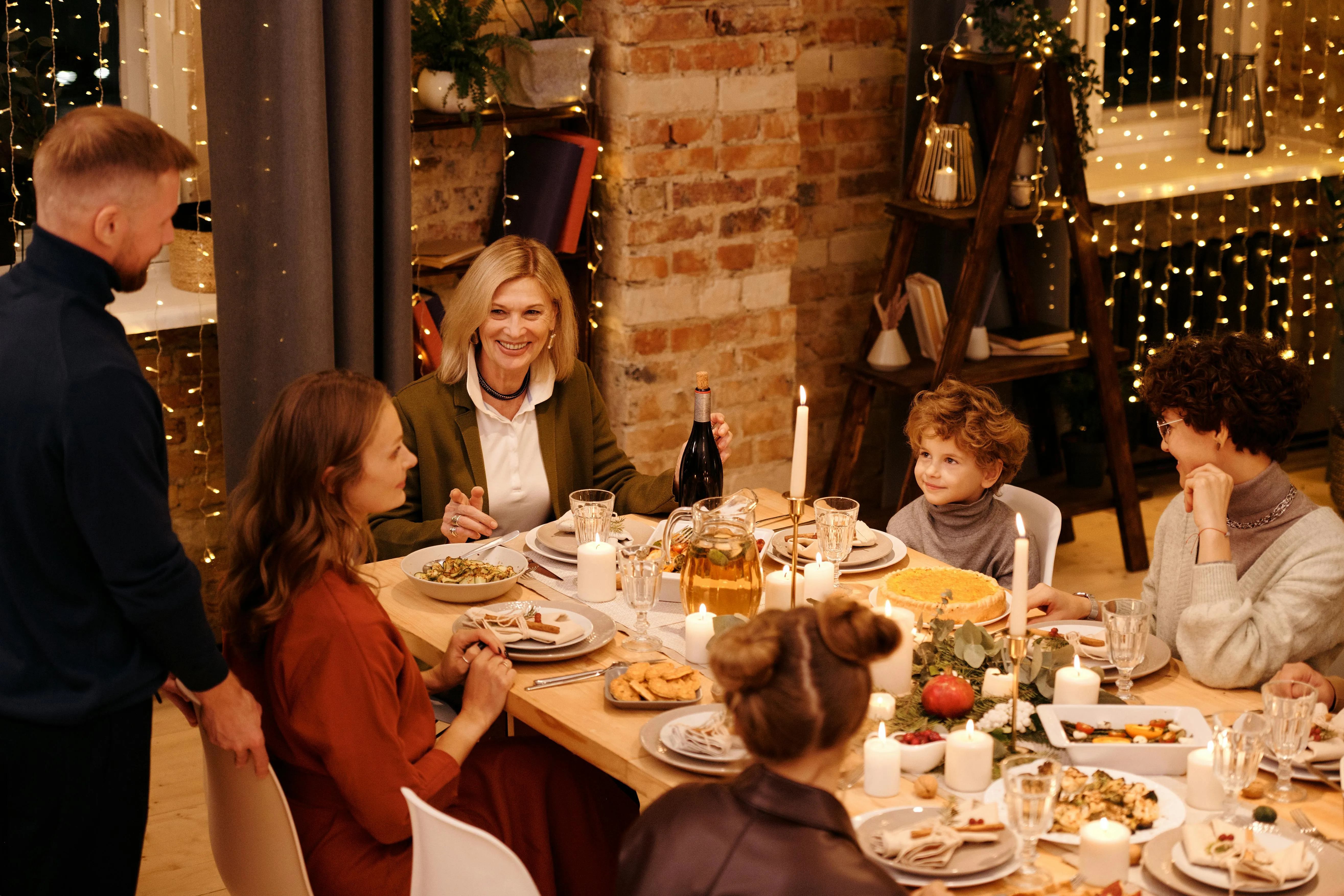 Family gathered around a candlelit dining table with food and drinks, smiling and engaging in conversation.