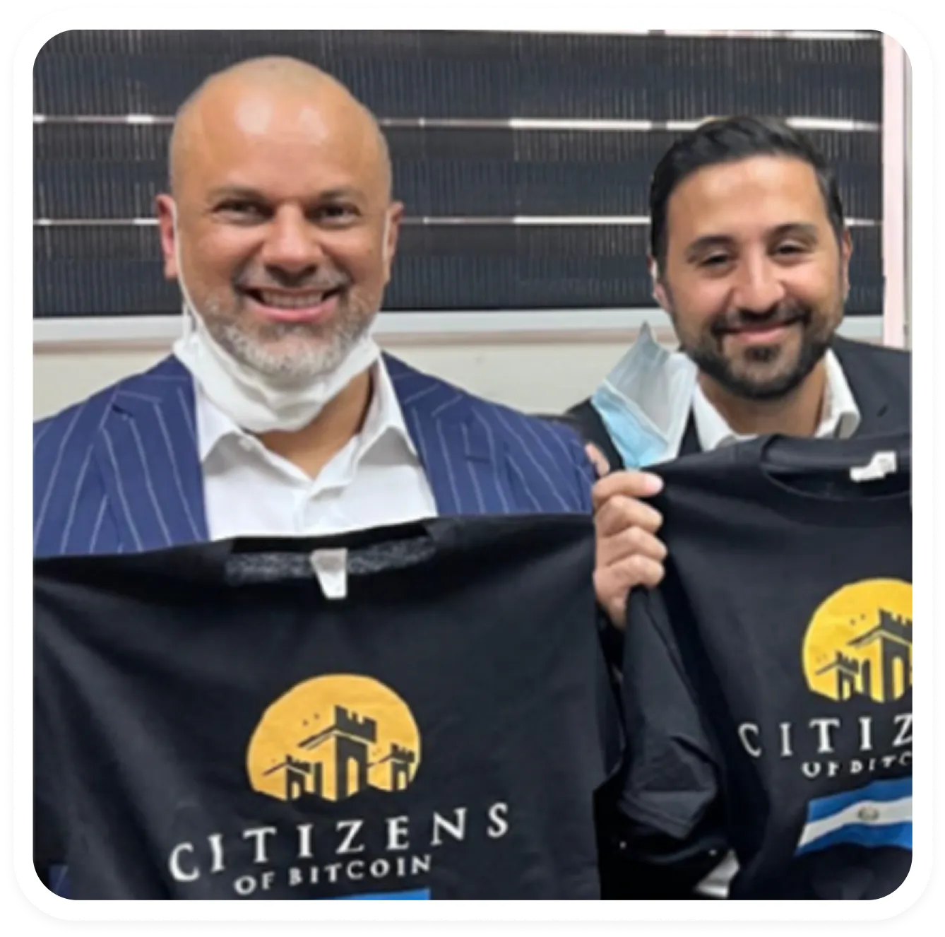 Two smiling men holding black T-shirts with a yellow logo and text reading 'Citizens of Bitcoin'.
