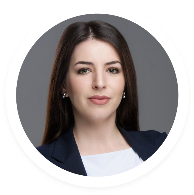Professional headshot of a woman with long dark hair, wearing a navy blazer and white top, against a gray background.
