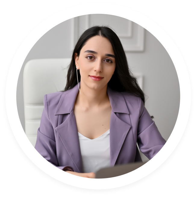 Woman with long dark hair wearing a lavender blazer and white top, seated indoors in front of a light background.