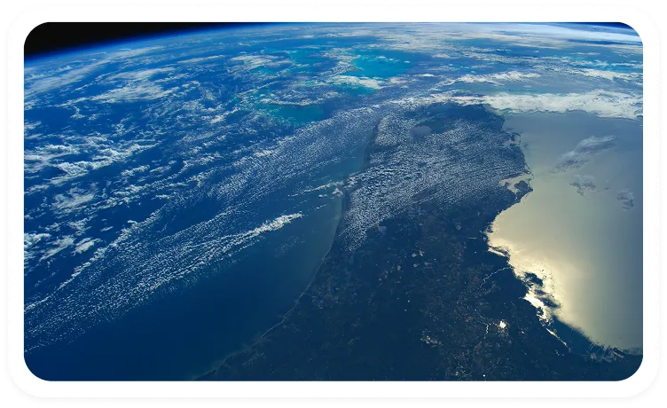 Satellite view of a large peninsula surrounded by ocean and cloudy sky, with sunlight reflecting on the water.