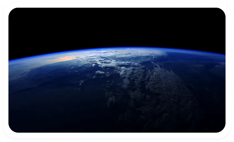 View of Earth from space showing a curved horizon with atmospheric glow and scattered clouds over dark land and ocean.