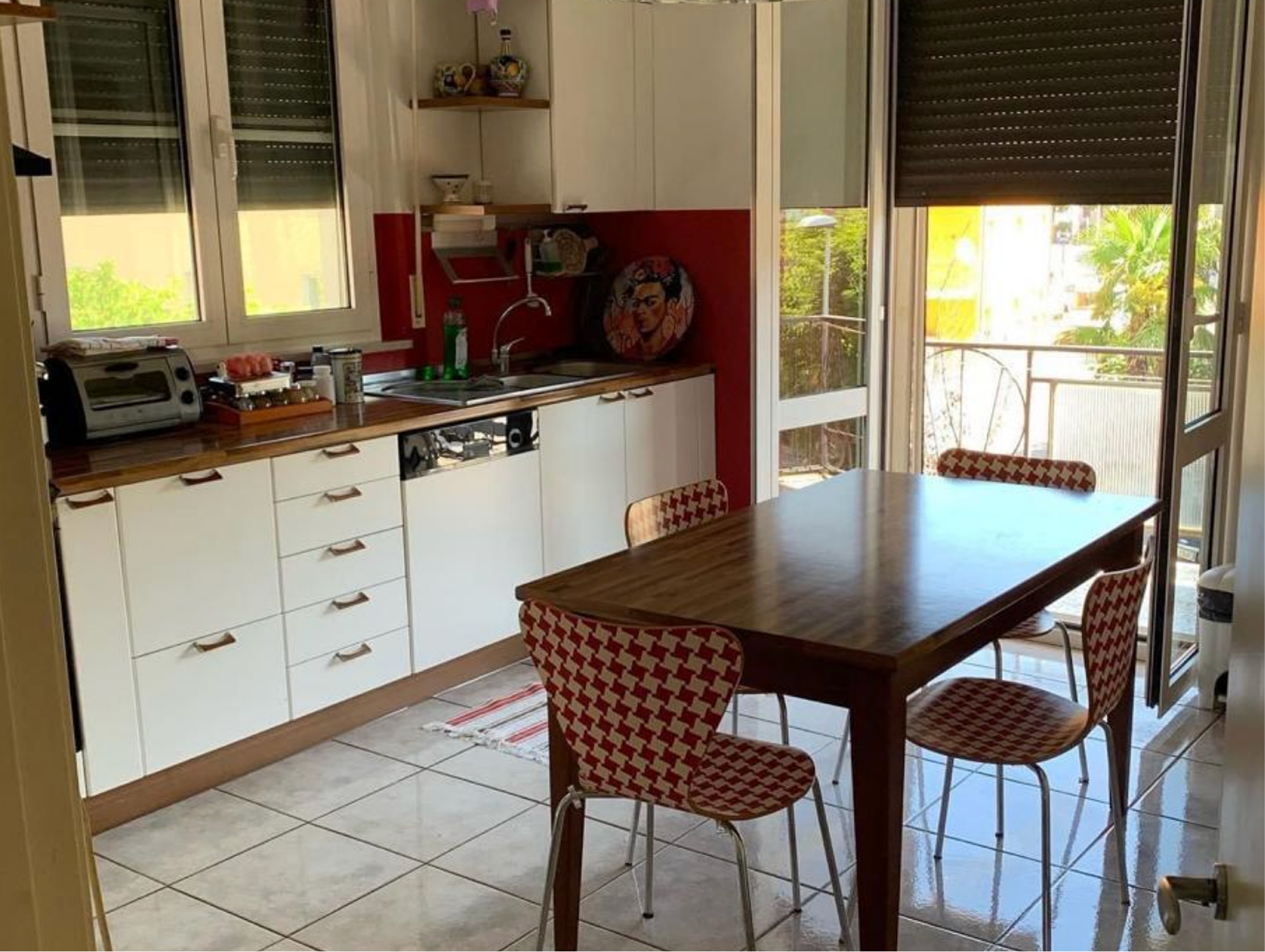 Kitchen with white cabinets, wooden countertop, a dining table with four patterned chairs, and a sliding glass door leading to a balcony.