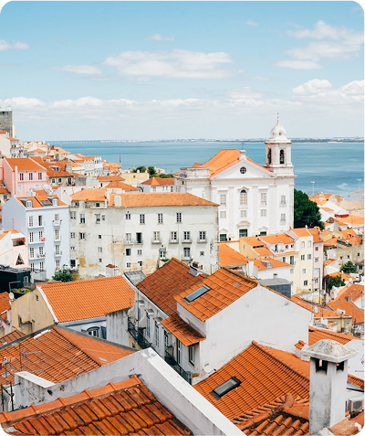 View of a coastal town with white and pastel buildings featuring red tile roofs under a blue sky with scattered clouds.