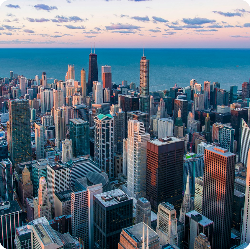 Aerial view of a dense city skyline with tall skyscrapers at sunset, Lake Michigan in the background.