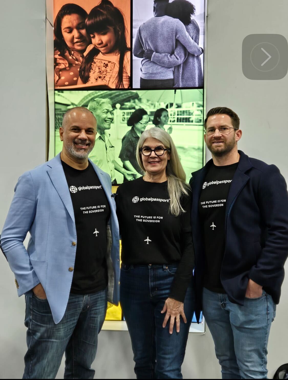 Three people wearing black Global Passport t-shirts stand smiling in front of a screen displaying diverse family photos.