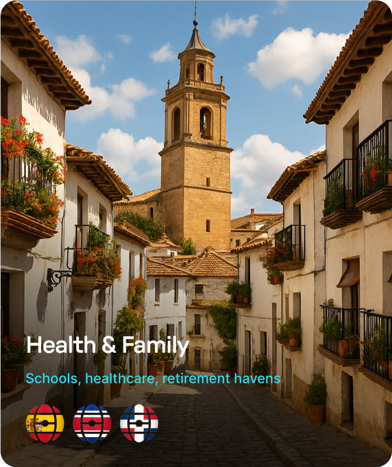 Sunlit narrow street in a Spanish village with white buildings, flower-filled balconies, and a tall stone church tower under a blue sky.