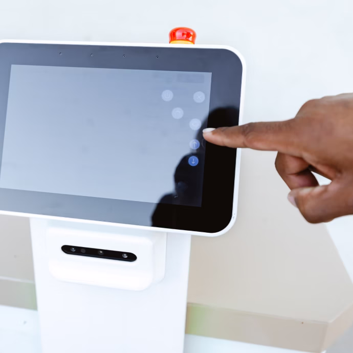 Person’s finger touching the screen of a white touchscreen control panel with an emergency stop button on top.