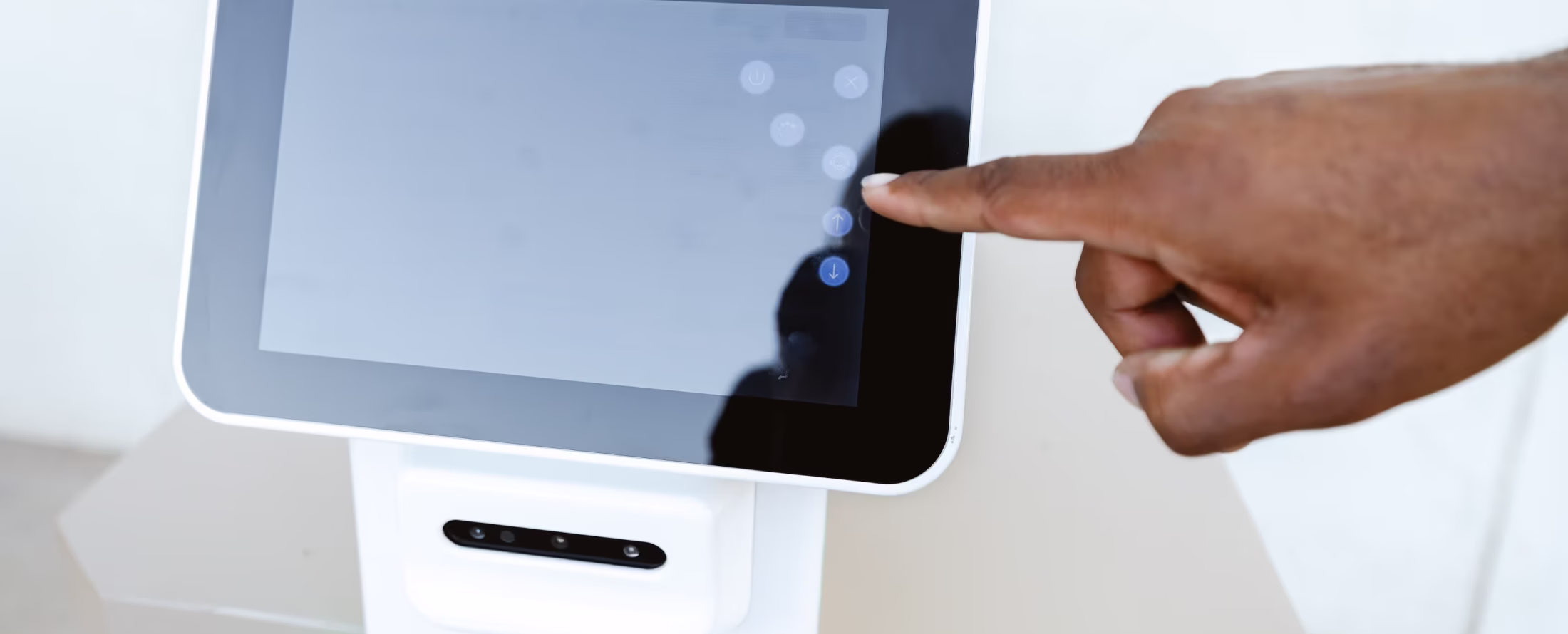 A hand with dark skin reaching to touch the up arrow button on a white touchscreen device.