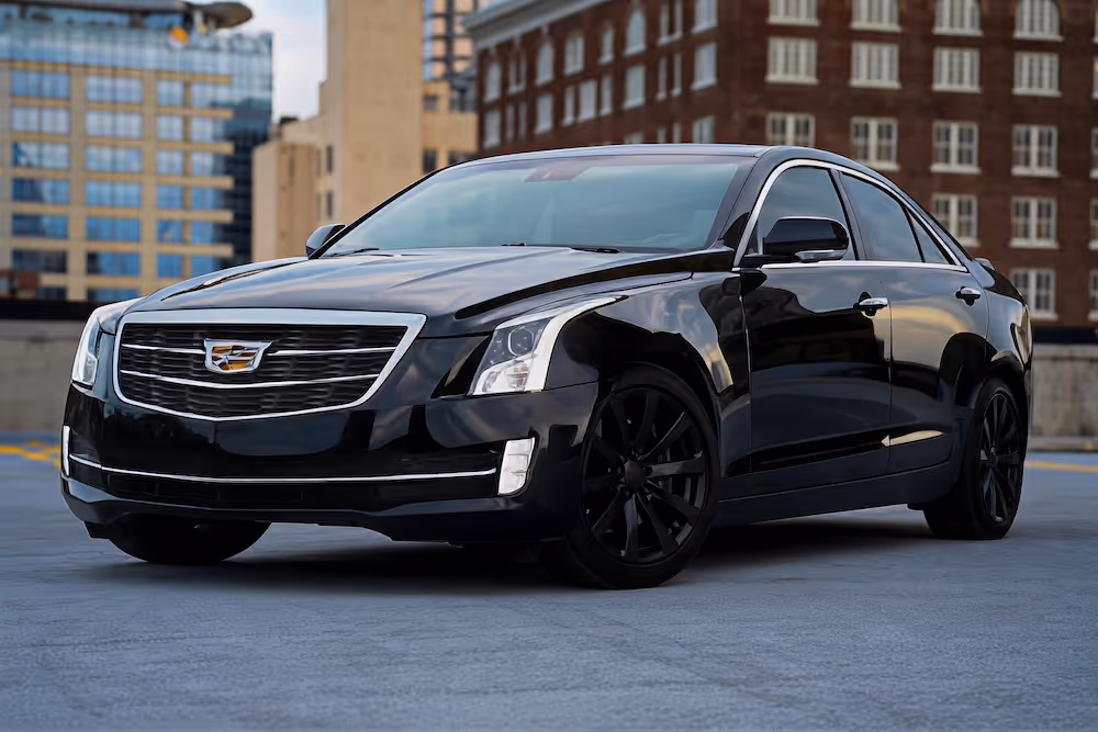 Black Cadillac sedan parked on rooftop with city buildings in the background.