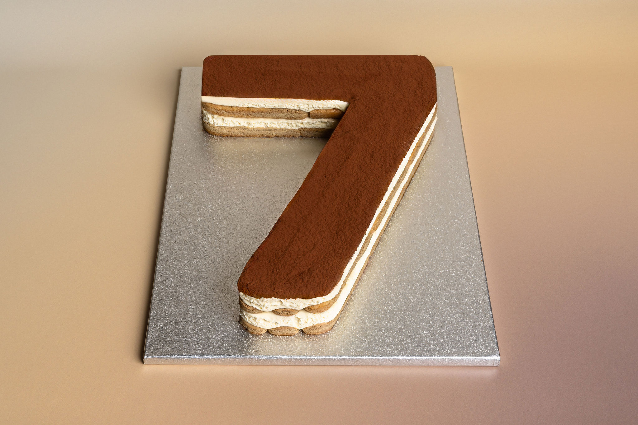 Layered tiramisu dessert shaped like the number 7 on a silver board.