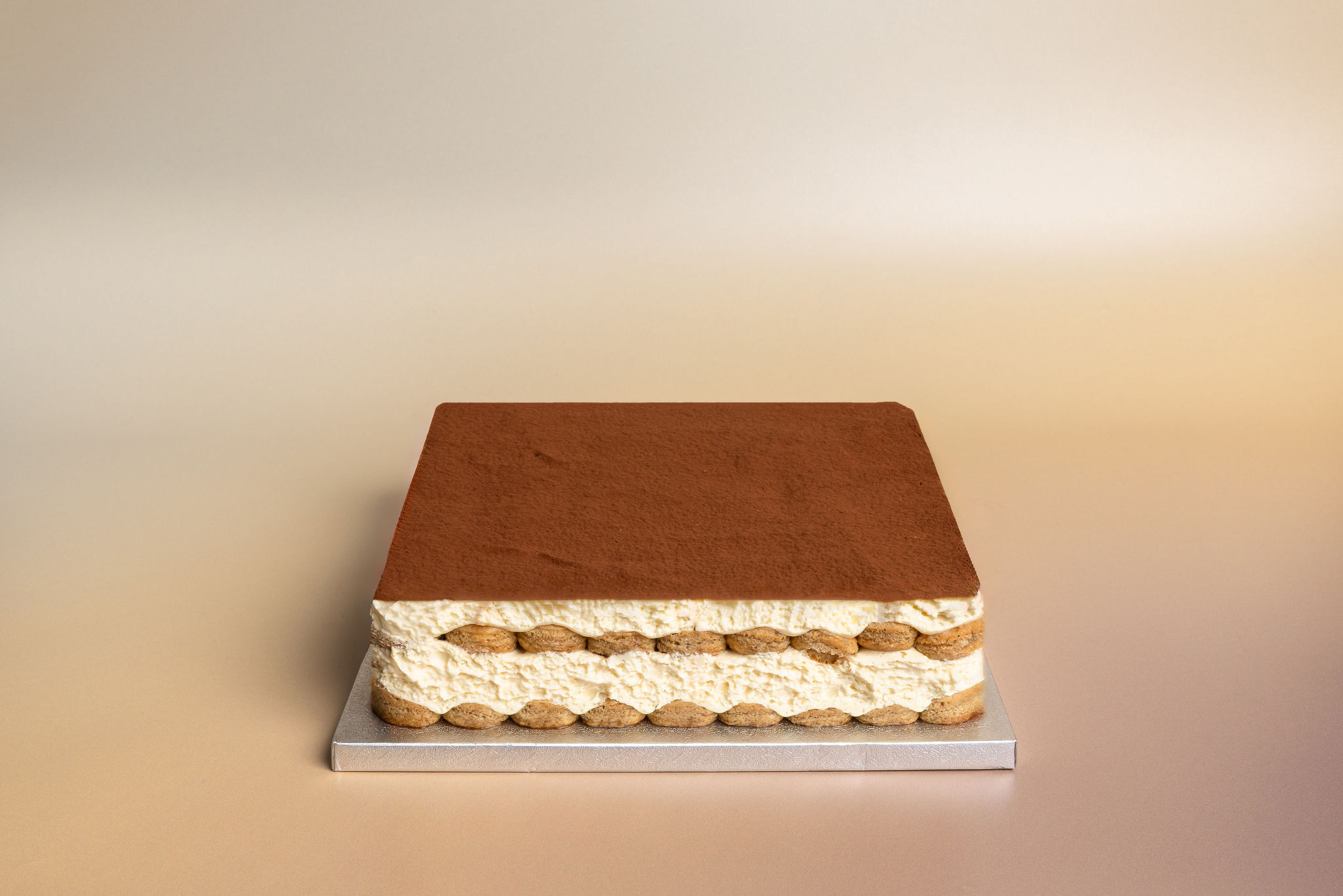 Rectangular tiramisu dessert with visible layers of cream and coffee-soaked ladyfingers topped with cocoa powder.
