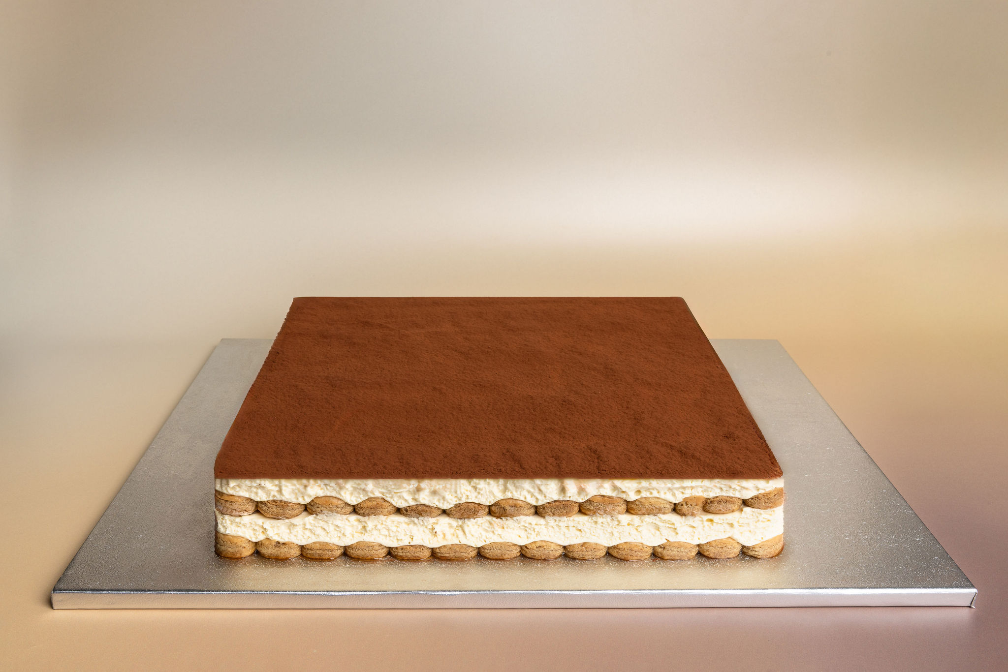 Square tiramisu dessert with cocoa powder on top and visible layers of cream and ladyfinger biscuits.