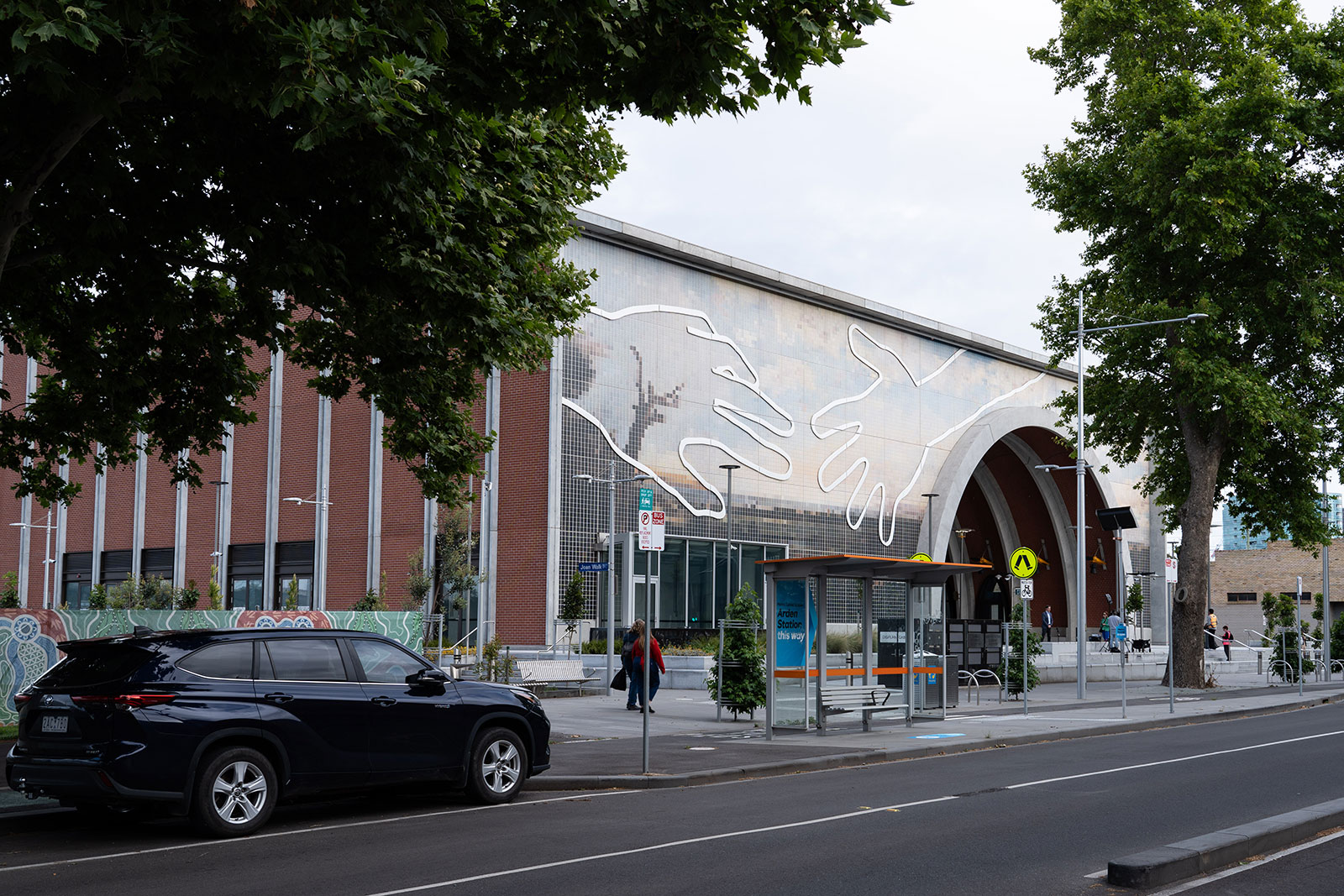Street view of Arden Station entrance with mural of large, outlined hands reaching towards each other on the building facade.
