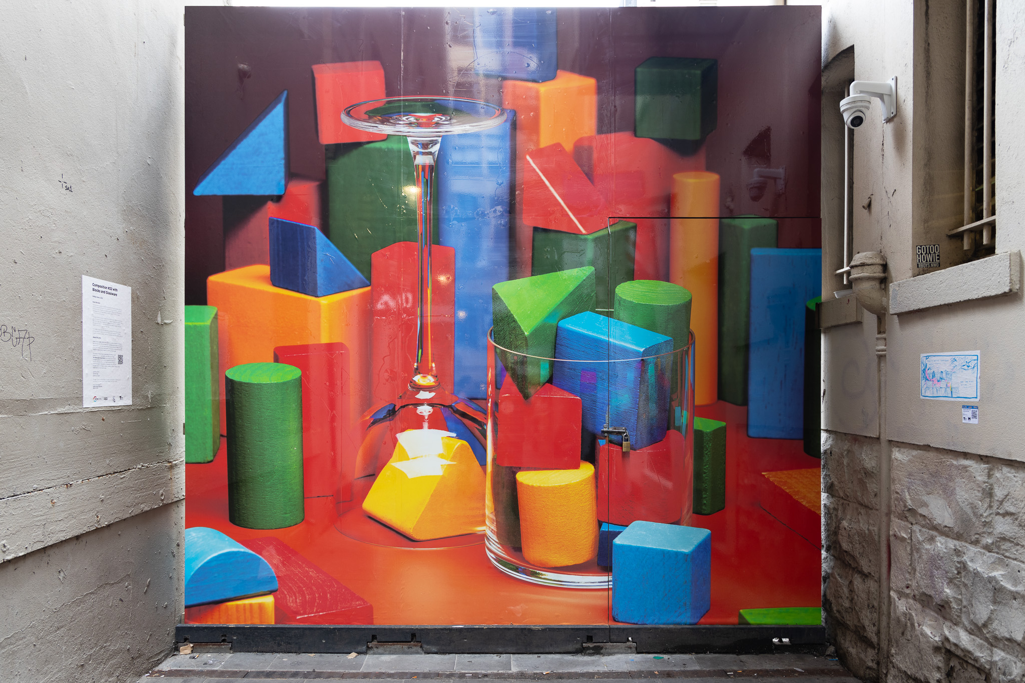 Colorful wooden geometric blocks arranged around and inside a transparent glass and an upside-down wine glass on a red surface. Artwork by Shelly Horan