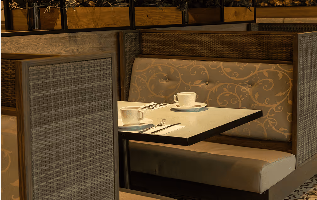 Cozy restaurant booth with patterned cushioned backrest and two cups on a set table.