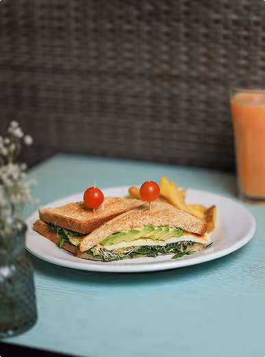 Club sandwich with lettuce, avocado, and tomato served with potato chips on a white plate.