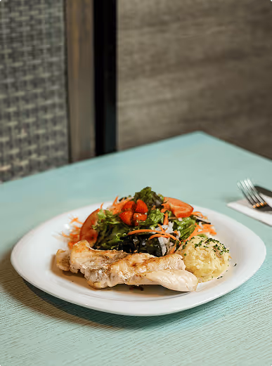 Plate with grilled chicken breast, mashed potatoes, and a mixed green salad with tomatoes and shredded carrots on a light blue table.