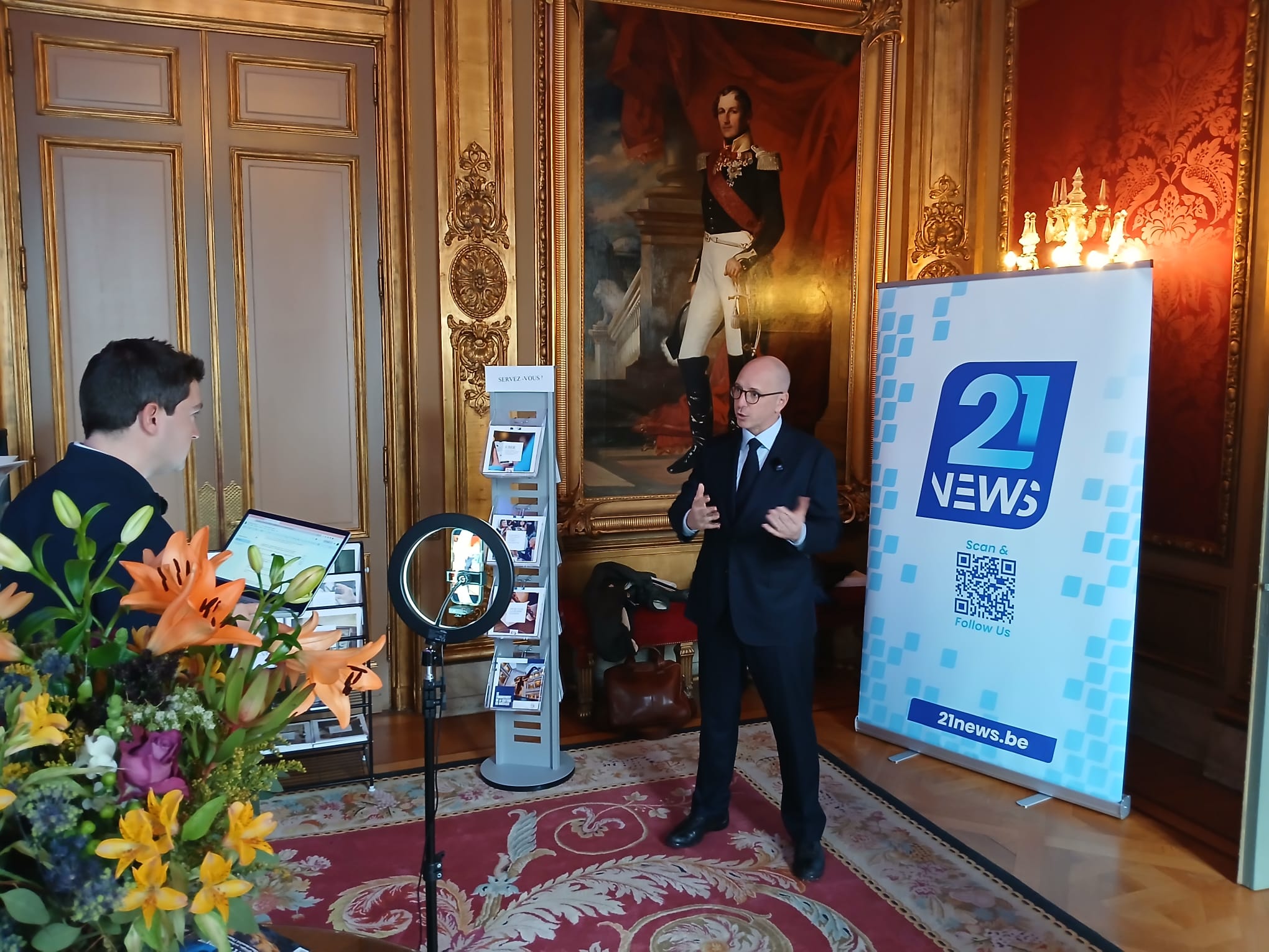 Interview de Benjamin Beeckmans (CEO de ByQwest) par le journaliste Harrison du Bus pour 21 News, au Palais d’Egmont à Bruxelles (Boulevard de Waterloo 31), devant le portrait du roi Léopold Ier, lors du colloque du Centre Jean Gol sur la souveraineté des paiements en Europe, avec dispositif de tournage (smartphone et ring light).