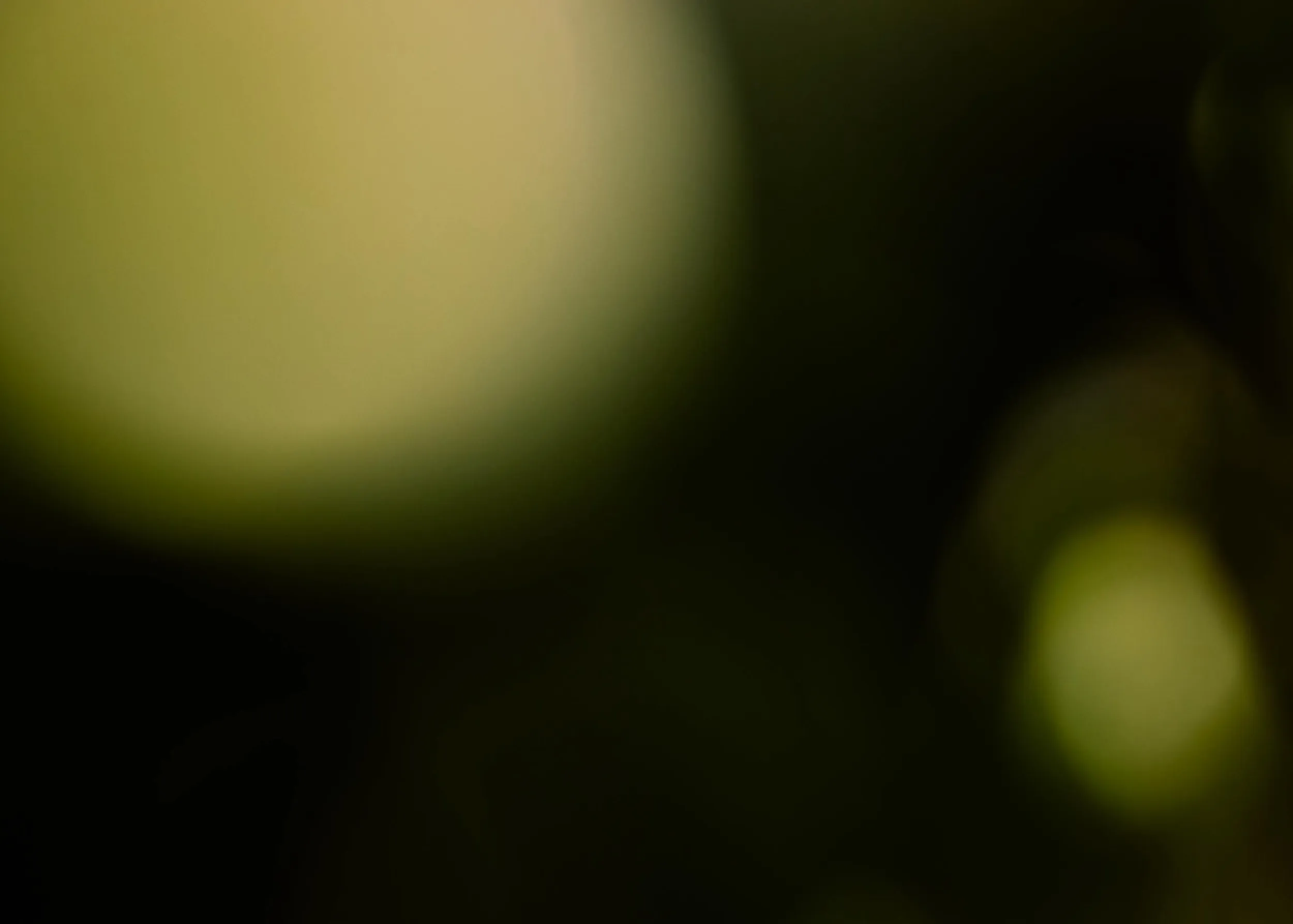Abstract dark background with soft green and yellow blurred light spots.