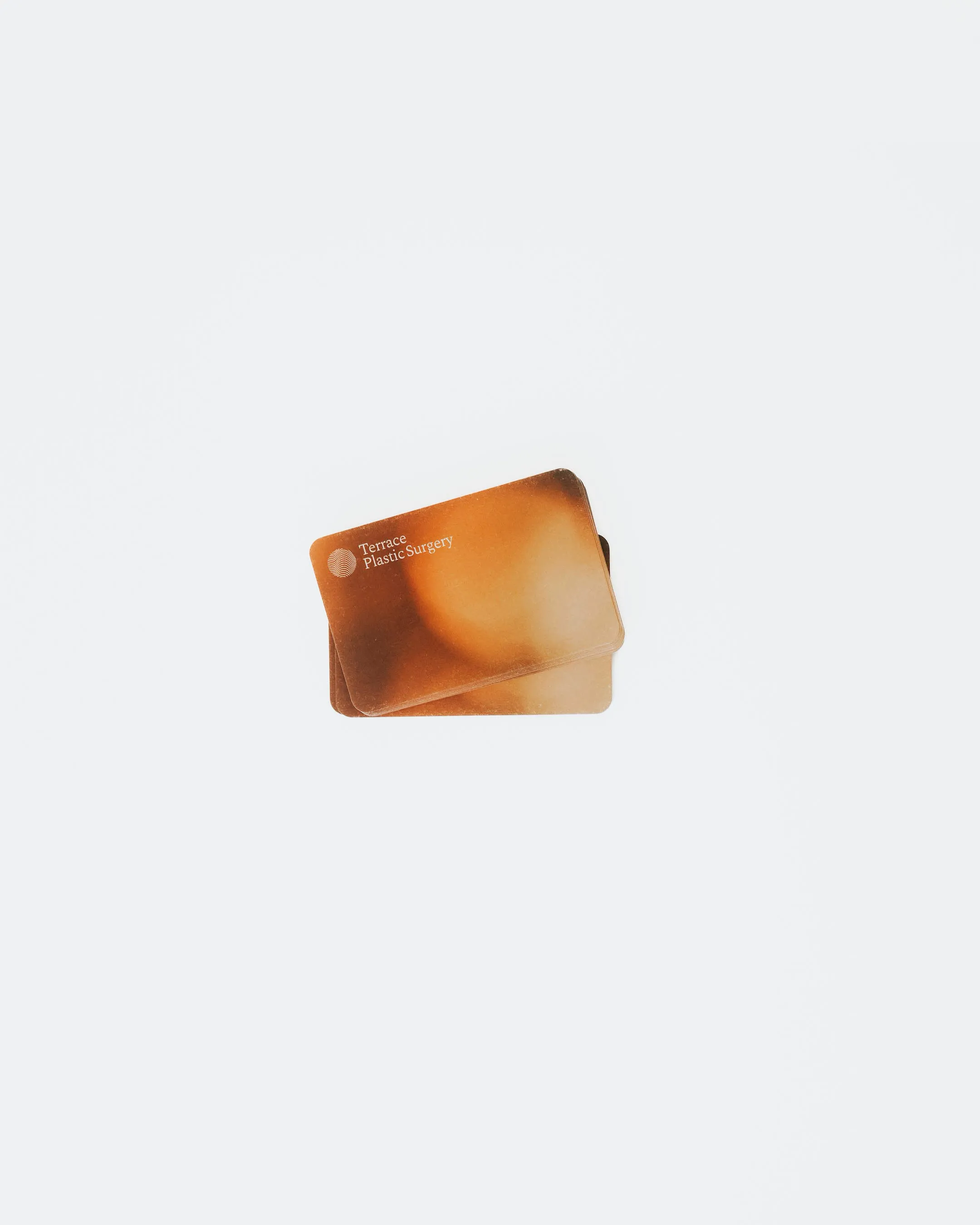 Two overlapping brown business cards with 'Terrace Plastic Surgery' text on a light background.