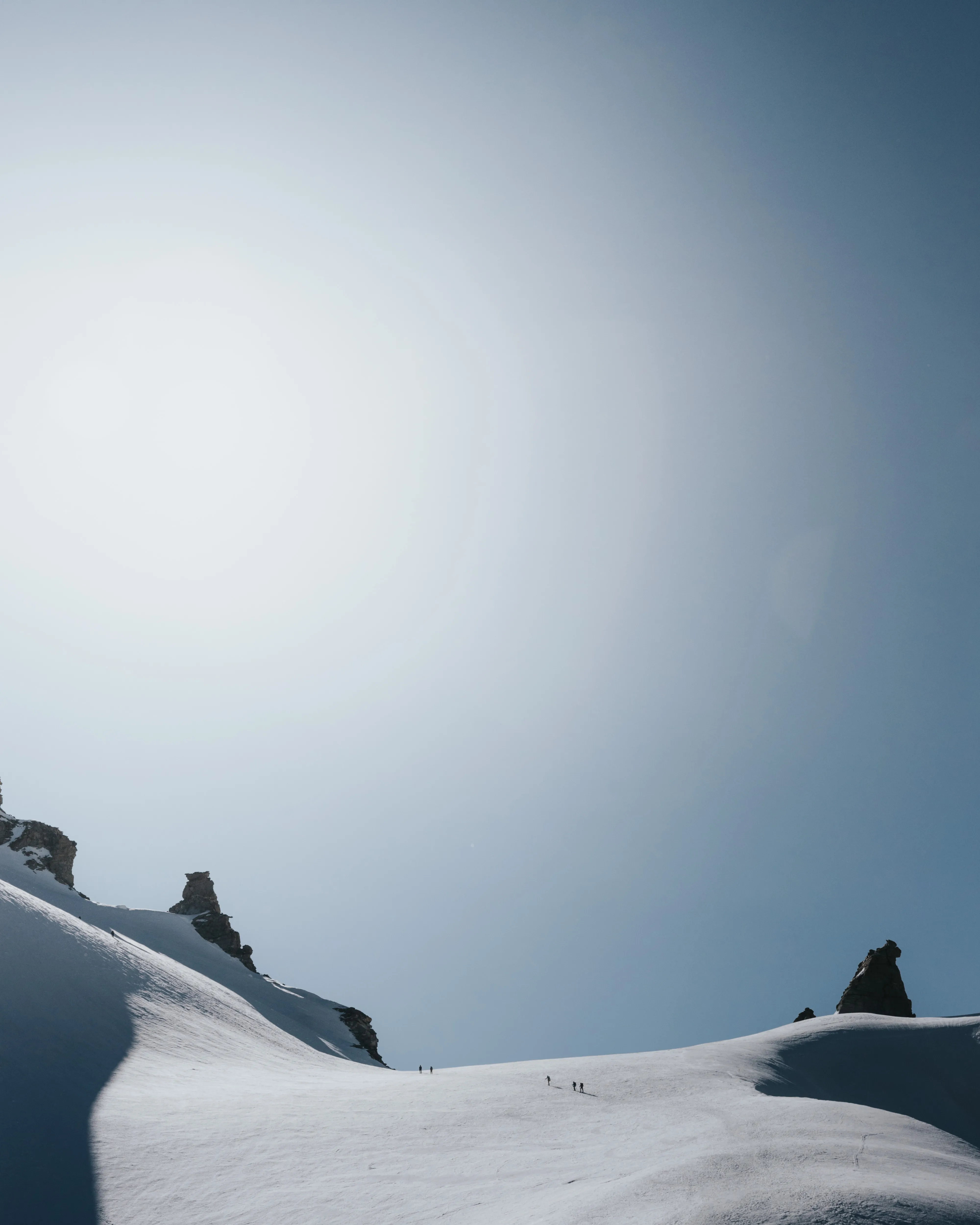 Small group of hikers walking on a snowy mountain ridge under a clear blue sky with bright sunlight.
