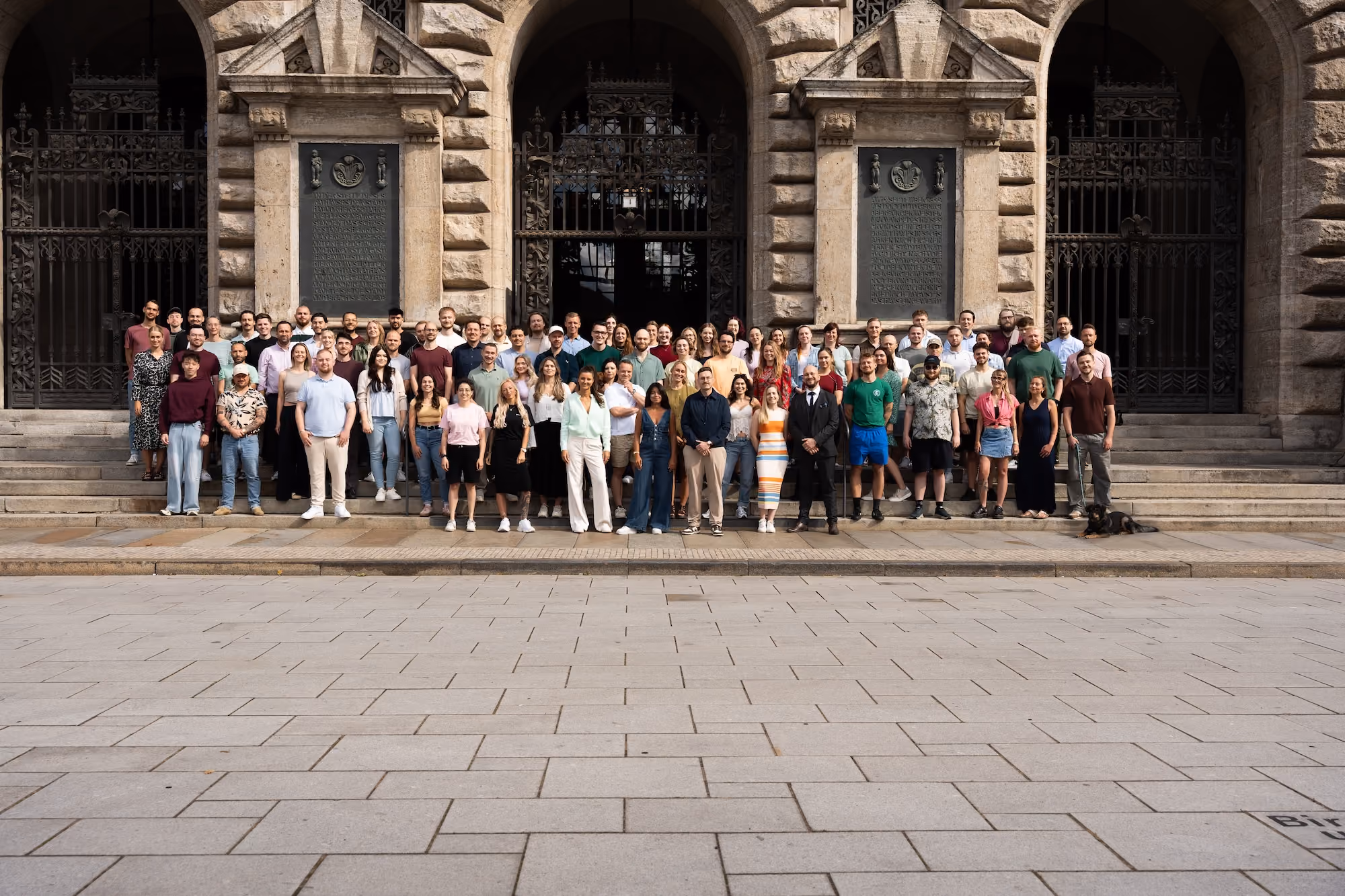 Große Gruppe von Menschen steht vor einem historischen Gebäude mit großen Bögen und Treppen.