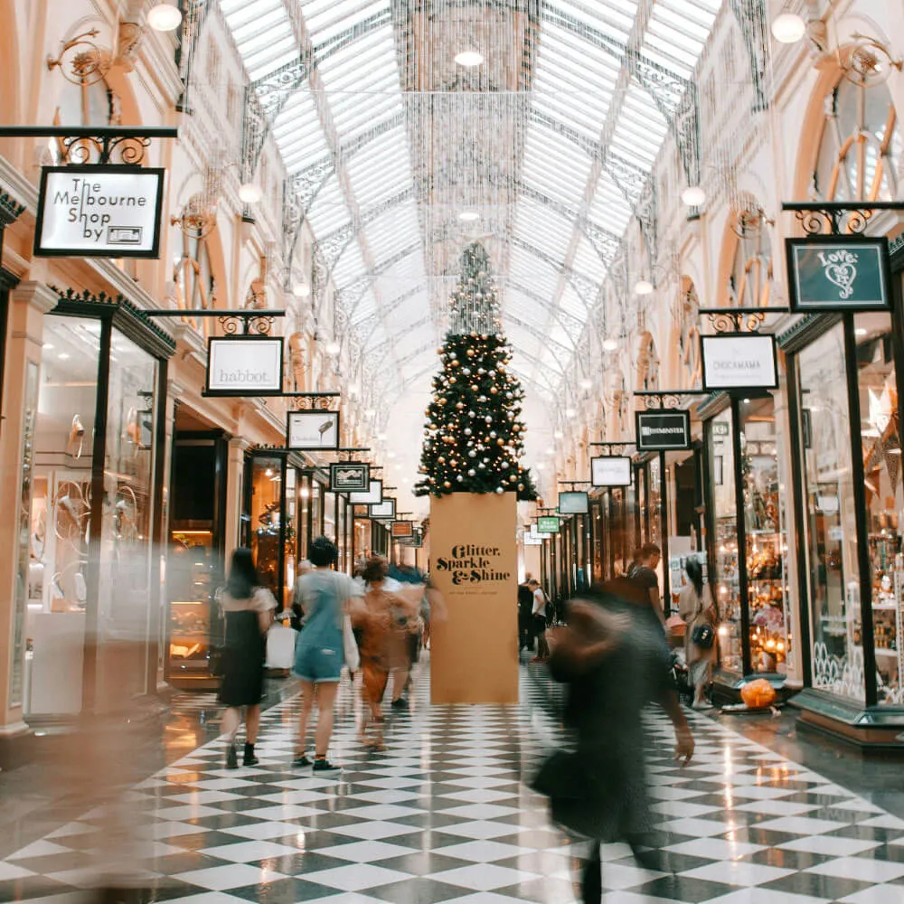 People walking inside a shopping arcade with checkered floor and a large decorated Christmas tree centerpiece.