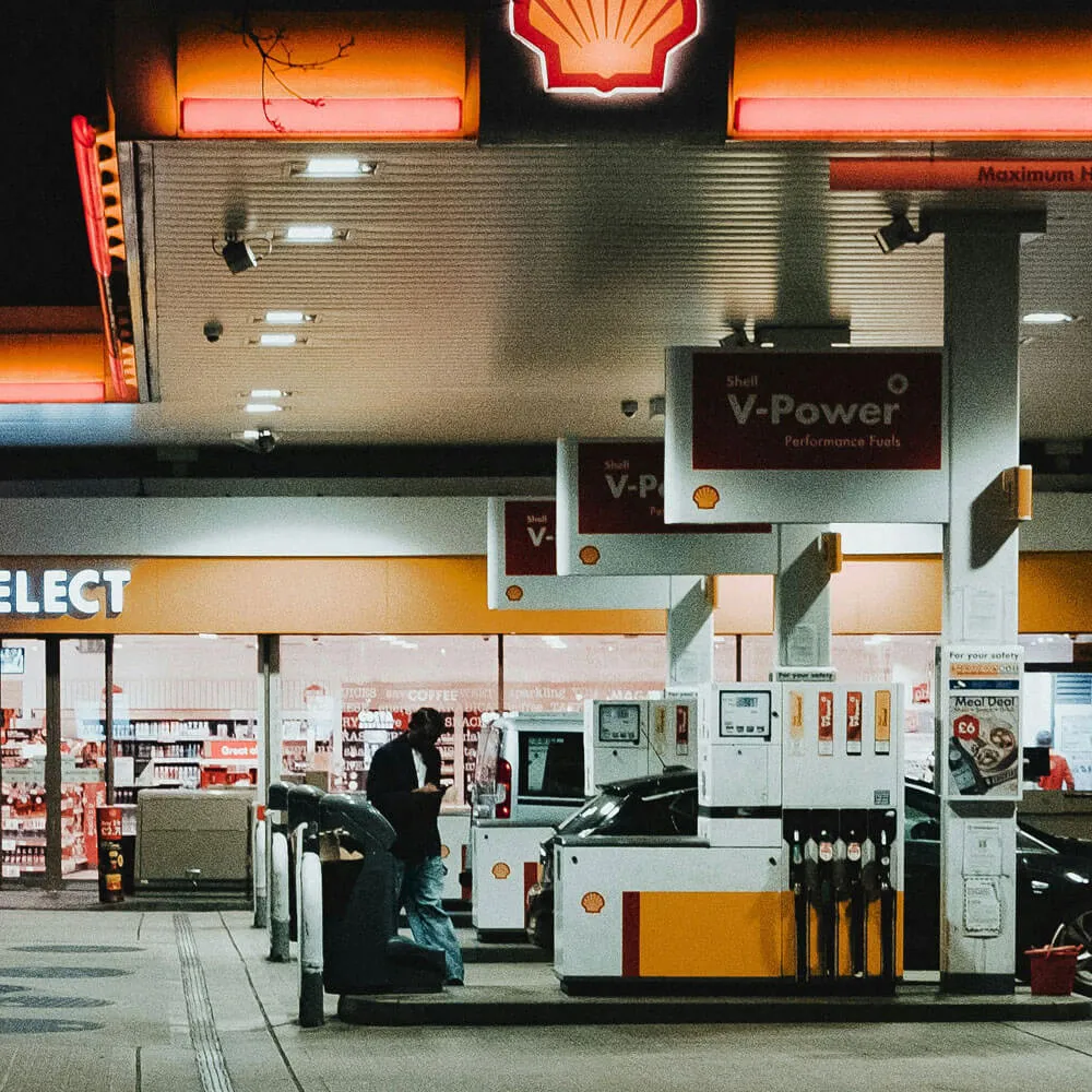 Night view of a Shell gas station with a man standing near the pump and cars refueling.