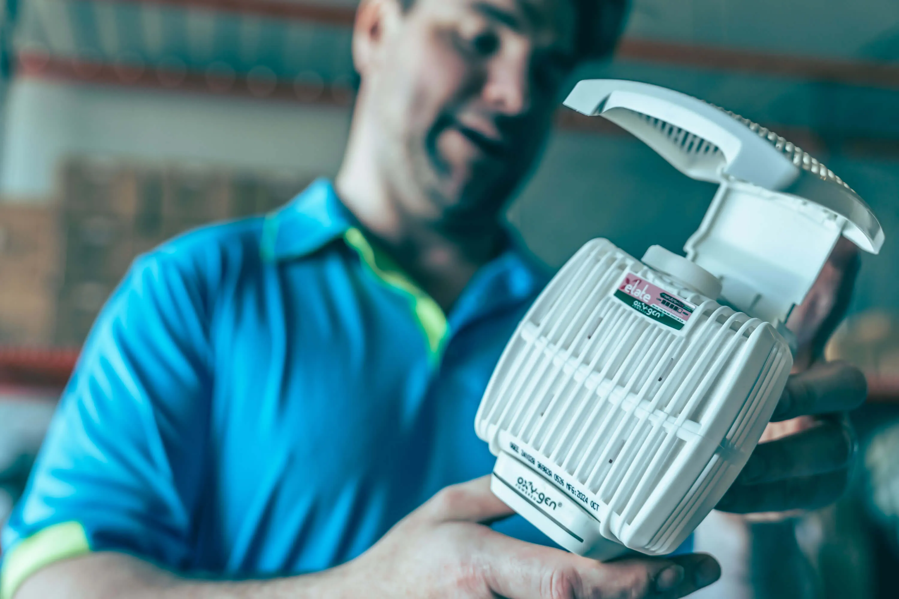 Man in blue shirt holding a white oxygen concentrator device labeled 'Oxygen'.