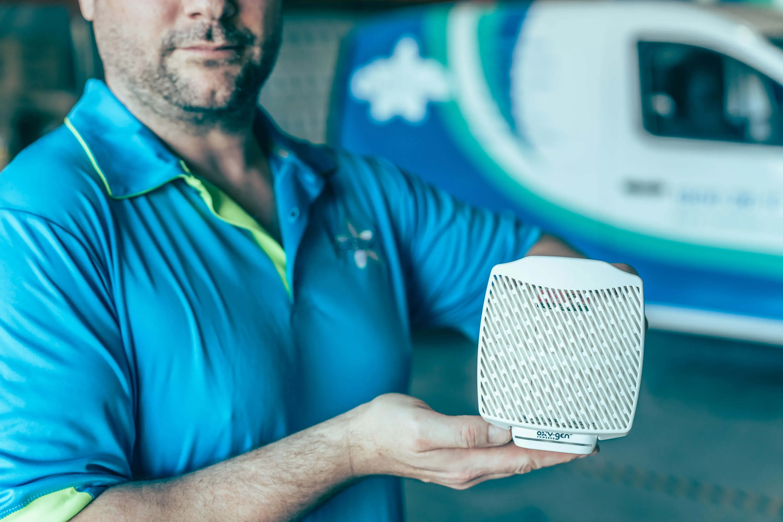 Man in blue shirt holding a white air purifier device with a company van blurred in the background.