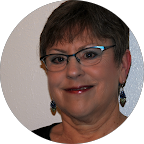 Headshot of a smiling woman with short brown hair, wearing glasses and dangly earrings.
